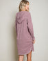 Woman wearing a mauve hooded dress against a plain background