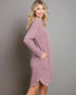 Woman wearing a mauve sweater dress against a gray background