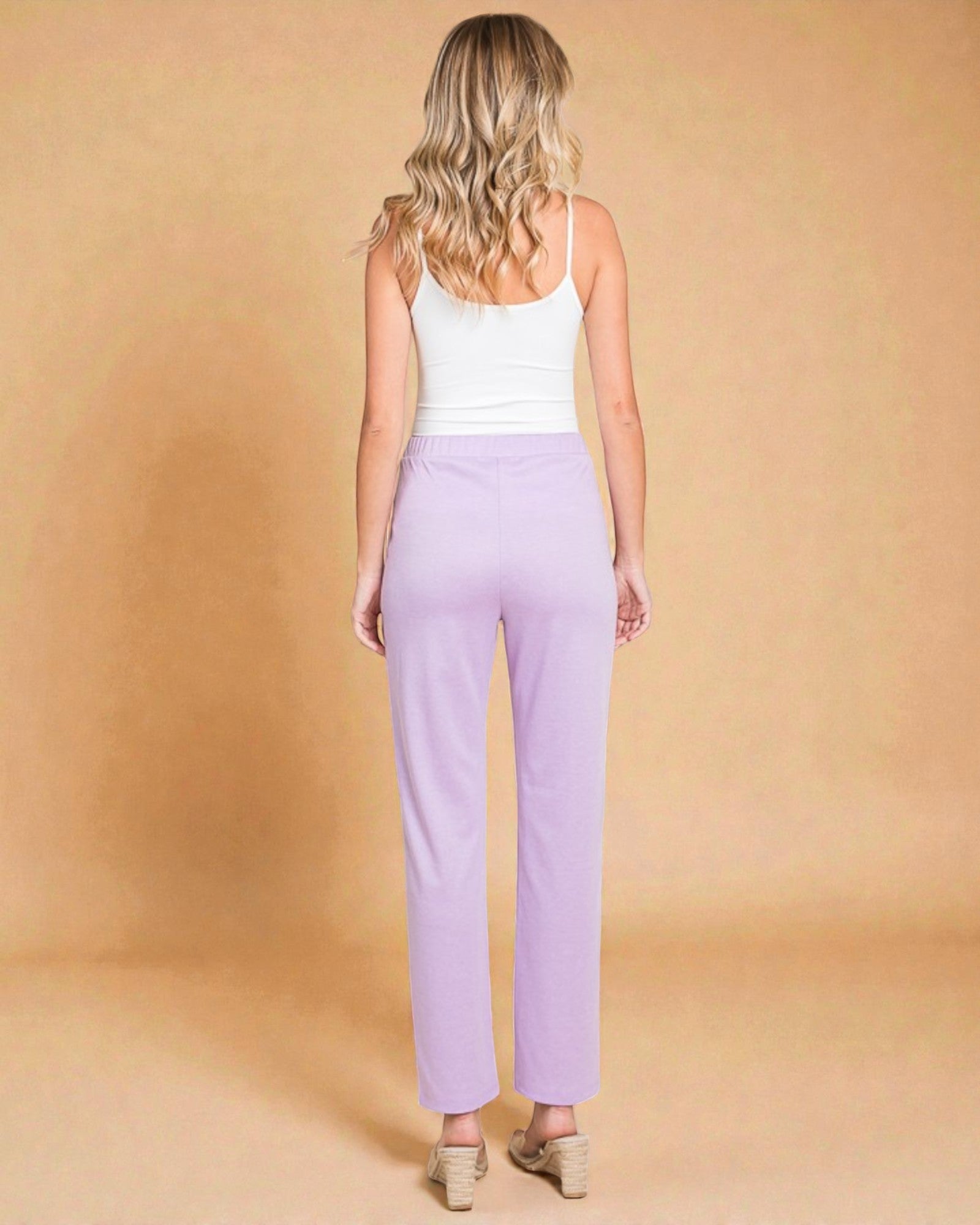 Woman wearing a white tank top and lavender pants against a beige background