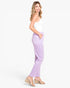 A woman modeling lavender cropped pants with side pockets, paired with a white tank top and beige wedge sandals, shown from a side profile against a plain white studio background.
