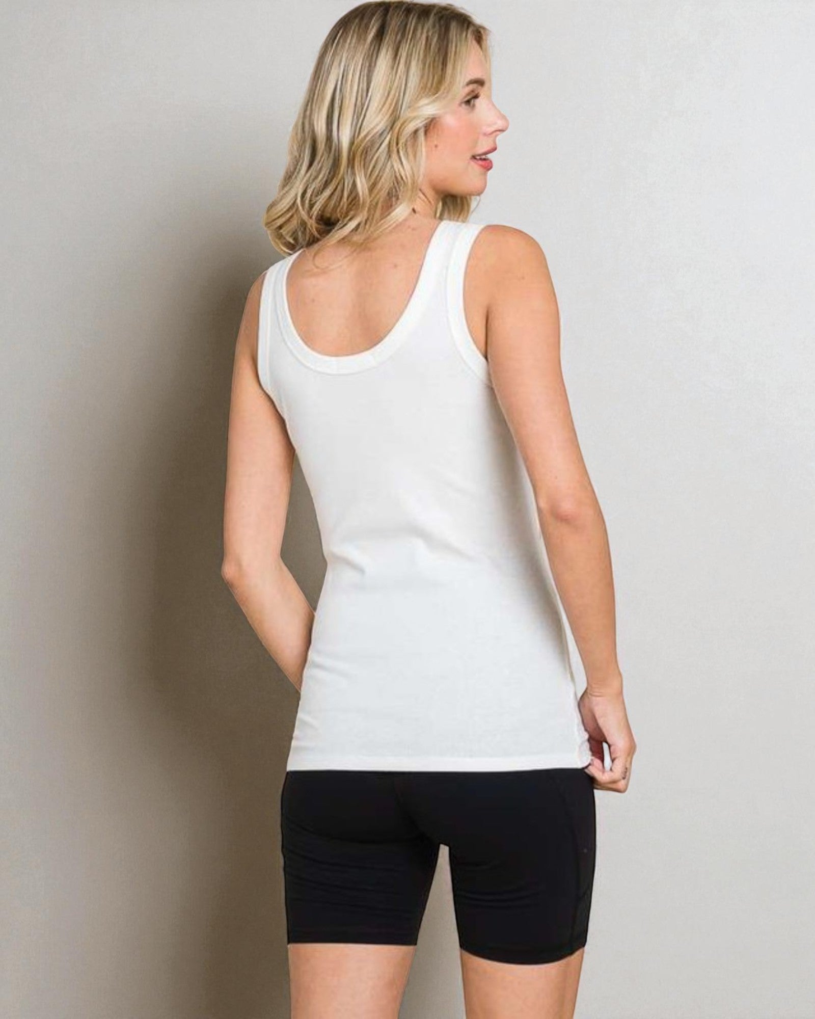 Woman wearing a white tank top and black shorts against a plain background