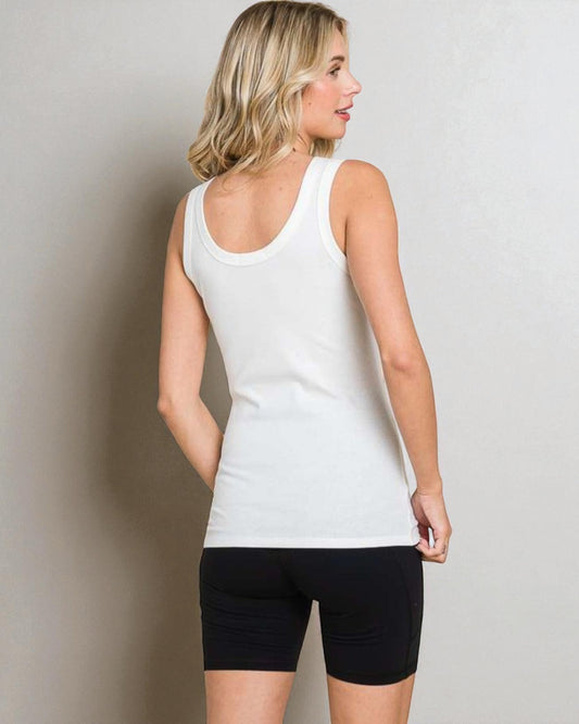 Woman wearing a white tank top and black shorts against a plain background