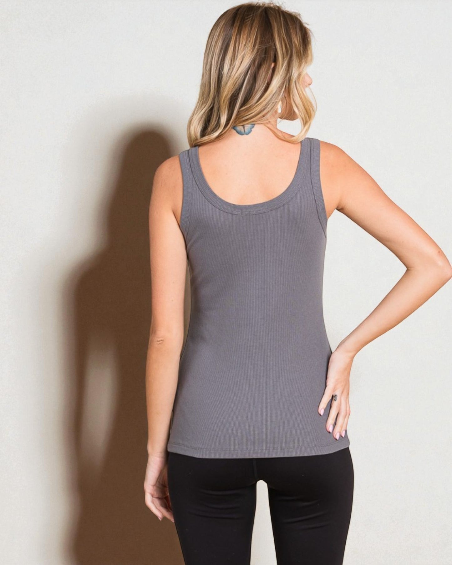 Woman wearing a gray tank top and black pants against a plain background