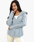 A woman wearing a light blue-gray ribbed zip-up hooded sweater over a white top and cream pants, photographed against a plain light gray studio background.