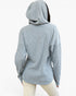 A person shown from the back wearing a light heather gray ribbed hoodie and cream pants against a plain white studio background.