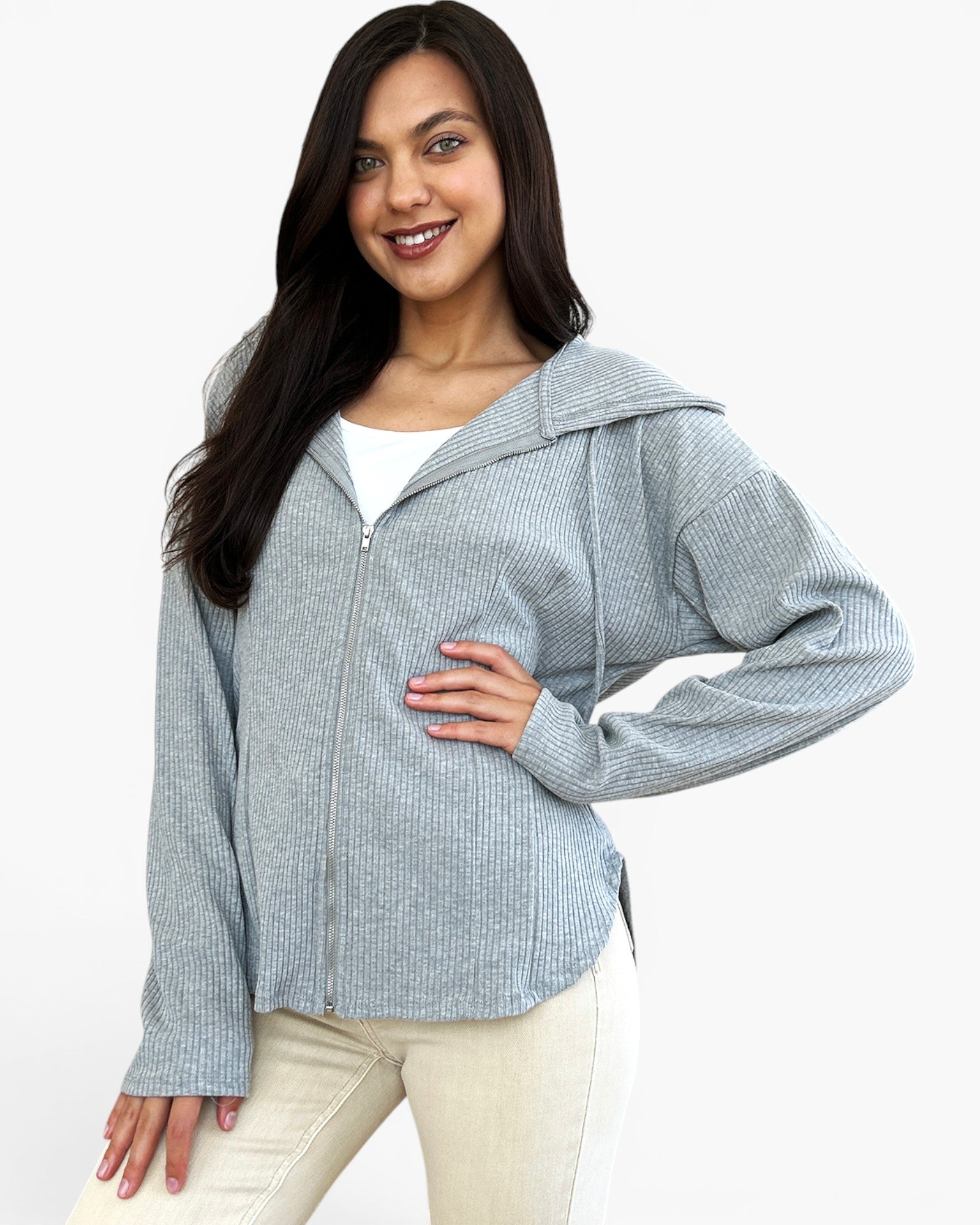 A woman modeling a light gray ribbed zip-up hoodie with a hood, worn over a white top and cream-colored pants, against a plain white background.
