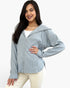 A woman modeling a light gray ribbed zip-up hoodie with a hood, worn over a white top and cream-colored pants, against a plain white background.