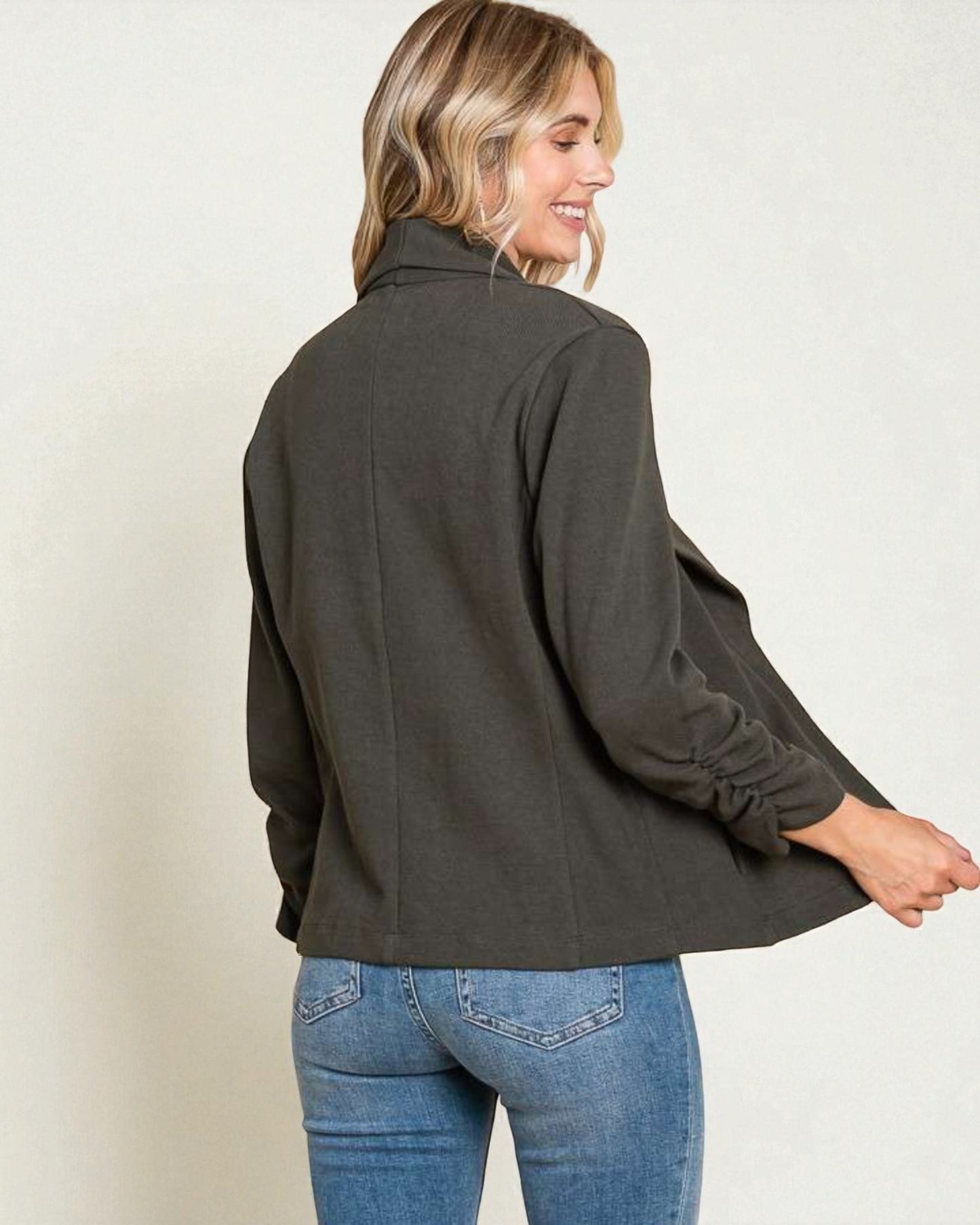 Woman wearing a dark gray jacket and blue jeans on a plain background