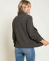 Woman wearing a dark gray jacket and blue jeans on a plain background