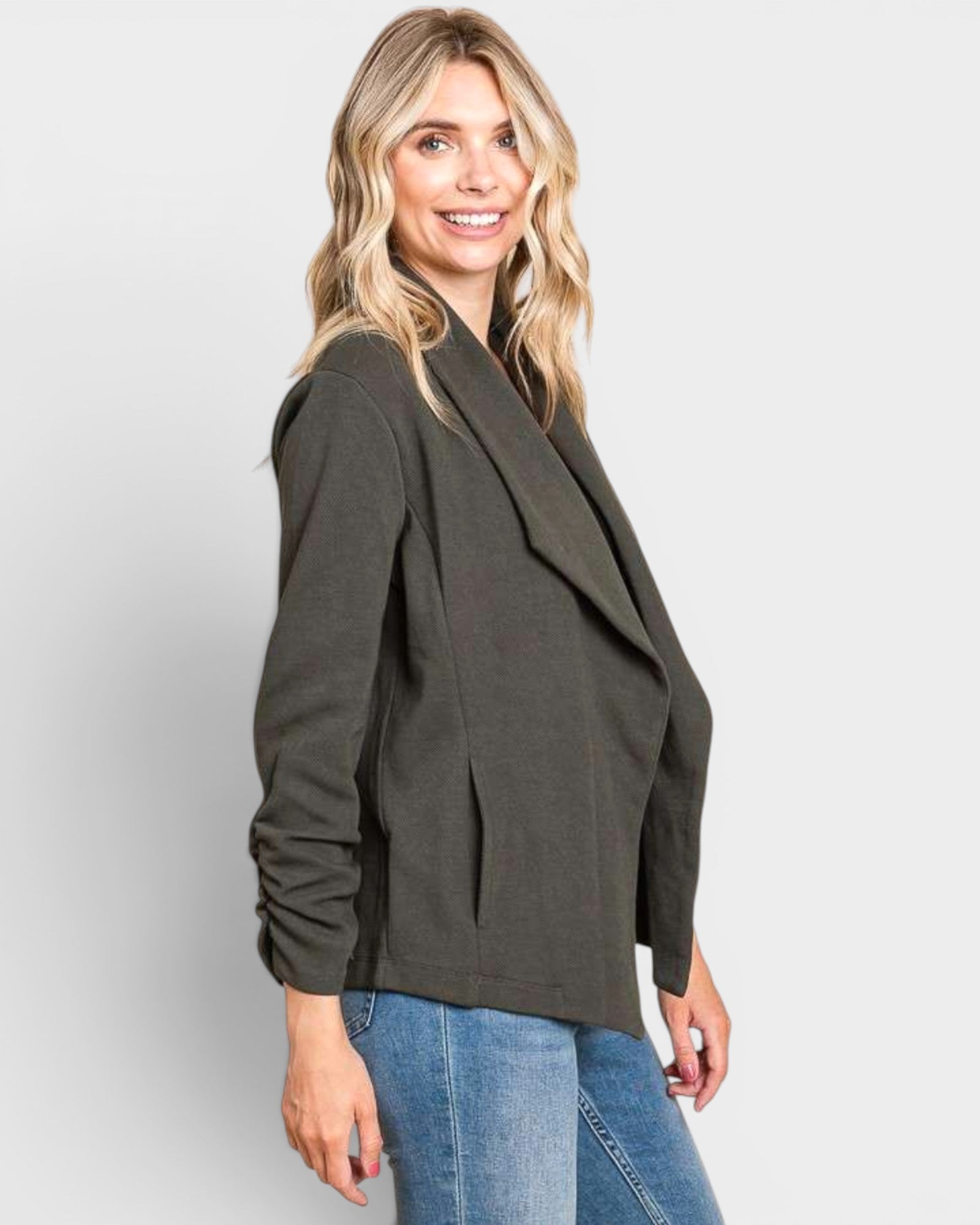 Woman wearing a green blazer and blue jeans on a light gray background