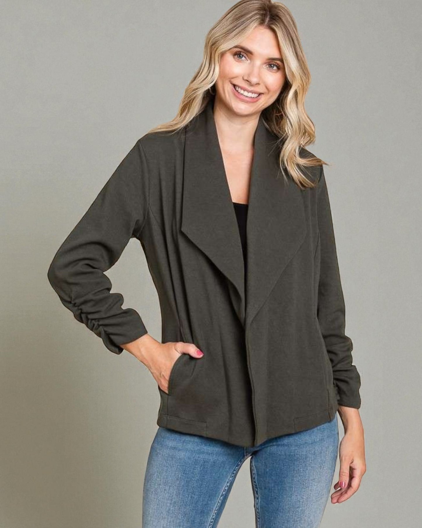 Woman wearing a dark green jacket and blue jeans on a gray background