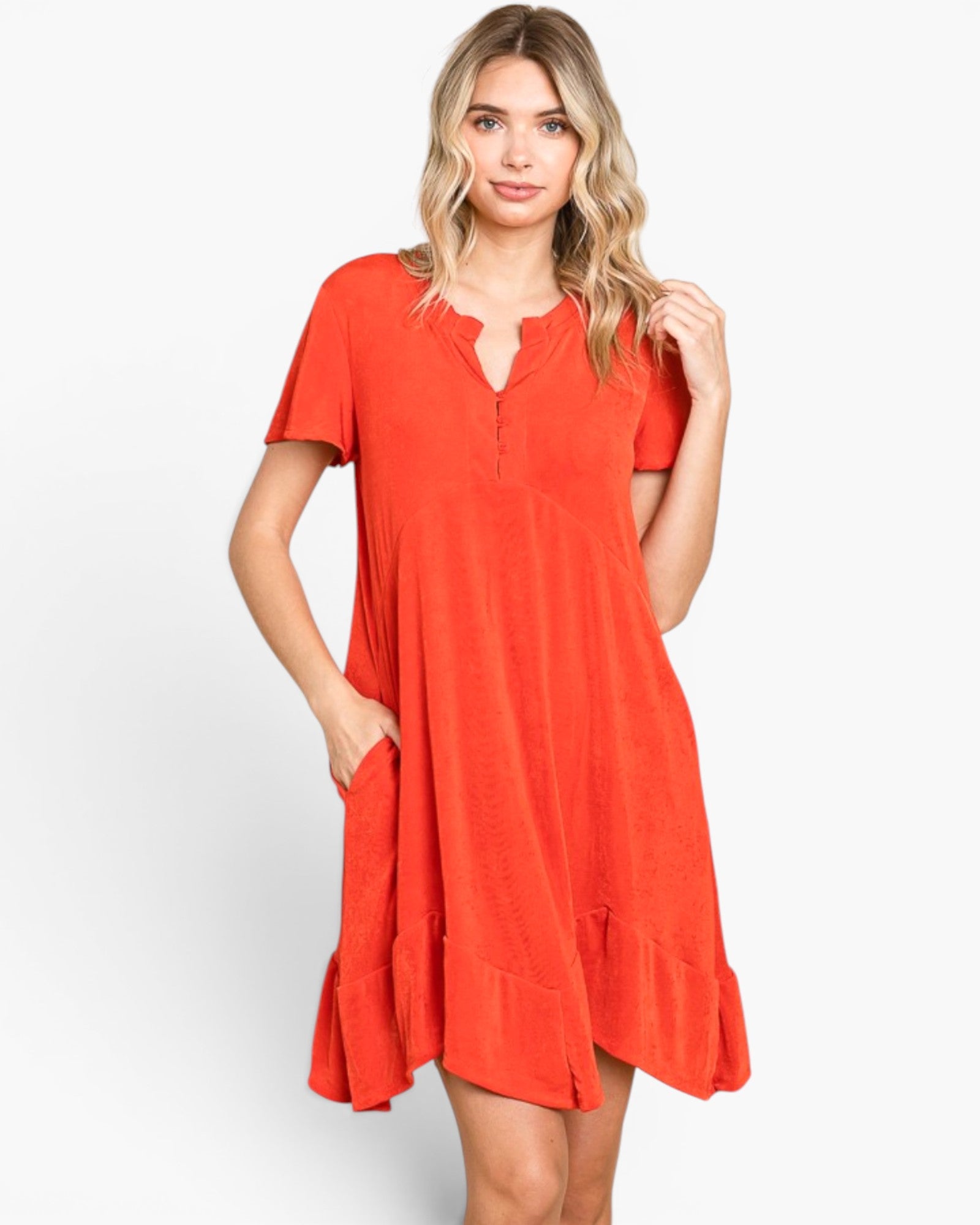 A woman modeling a short-sleeve orange dress with a split neckline, button detail, and side pockets against a light gray studio background.