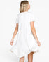 A woman shown from the back wearing a white short-sleeve dress with a ruffled hem, photographed against a plain light gray studio background.
