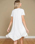 Woman wearing a white dress with ruffled hem against a beige wall.