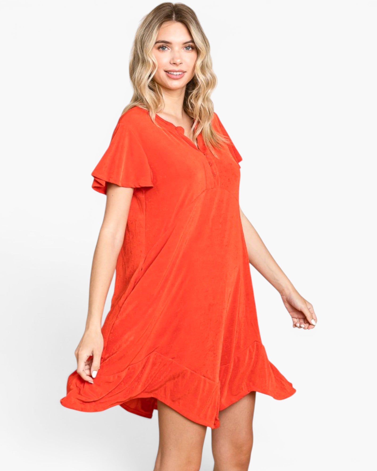 A woman modeling a bright orange short-sleeve tunic dress with a scalloped V-neckline and a flared hem, set against a plain light gray studio background.