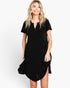 A woman modeling a short-sleeve black dress with a split V-neckline and a tiered ruffled hem, set against a plain light gray studio background.