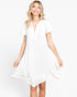 A woman wearing a white short-sleeve V-neck dress with a tiered ruffle hem, photographed against a clean white studio background.
