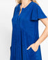 A woman wearing a royal blue short-sleeve tunic dress with a split V-neckline and side pockets, shown against a plain light gray background.