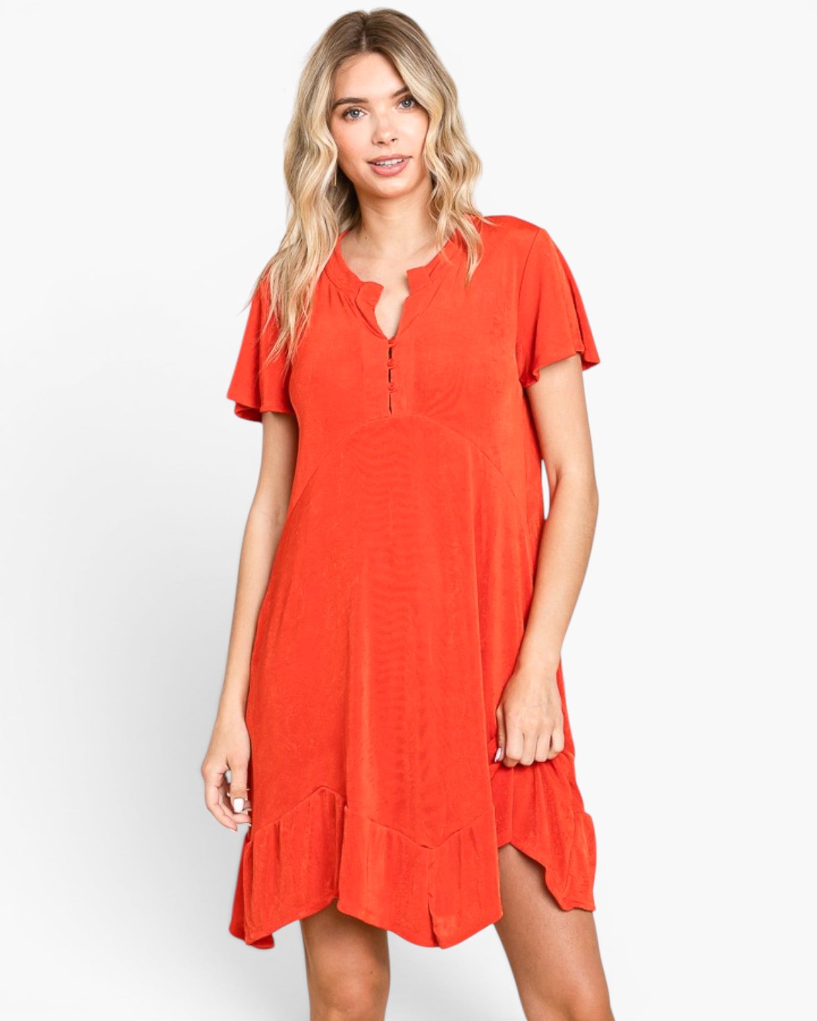 A woman modeling a short-sleeve orange-red dress with a split neckline, button detail, and ruffled hem against a plain light gray background.