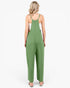 A woman viewed from behind wearing a sage green sleeveless jumpsuit with wide legs and thin shoulder straps, paired with a white tank top and white slide sandals, against a plain white background.