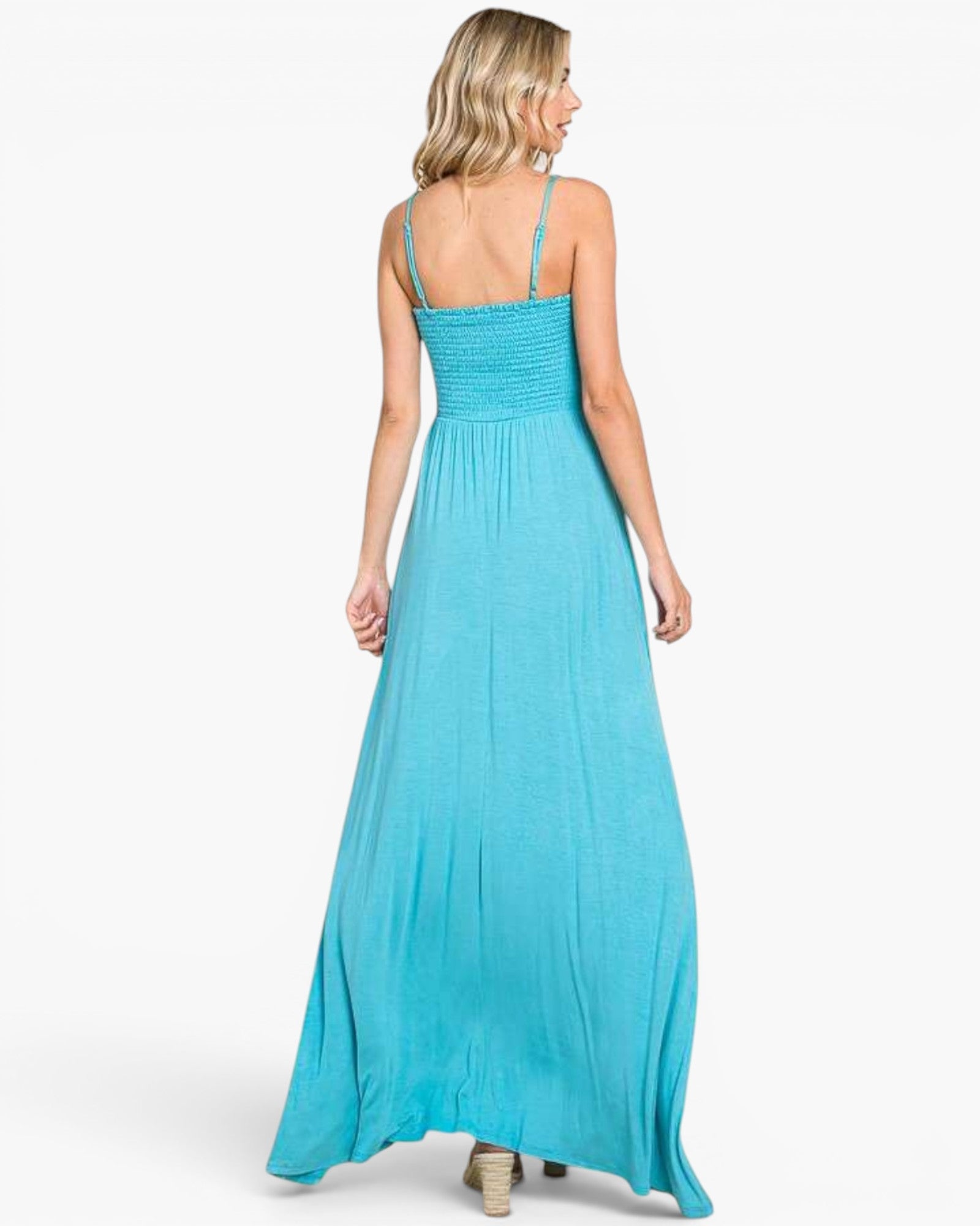 A woman modeling a bright turquoise blue maxi dress from the back, showing the smocked bodice and thin spaghetti straps against a clean white background.