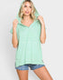 A woman wearing a light green and white striped hooded t-shirt with denim shorts, posing against a light gray background.