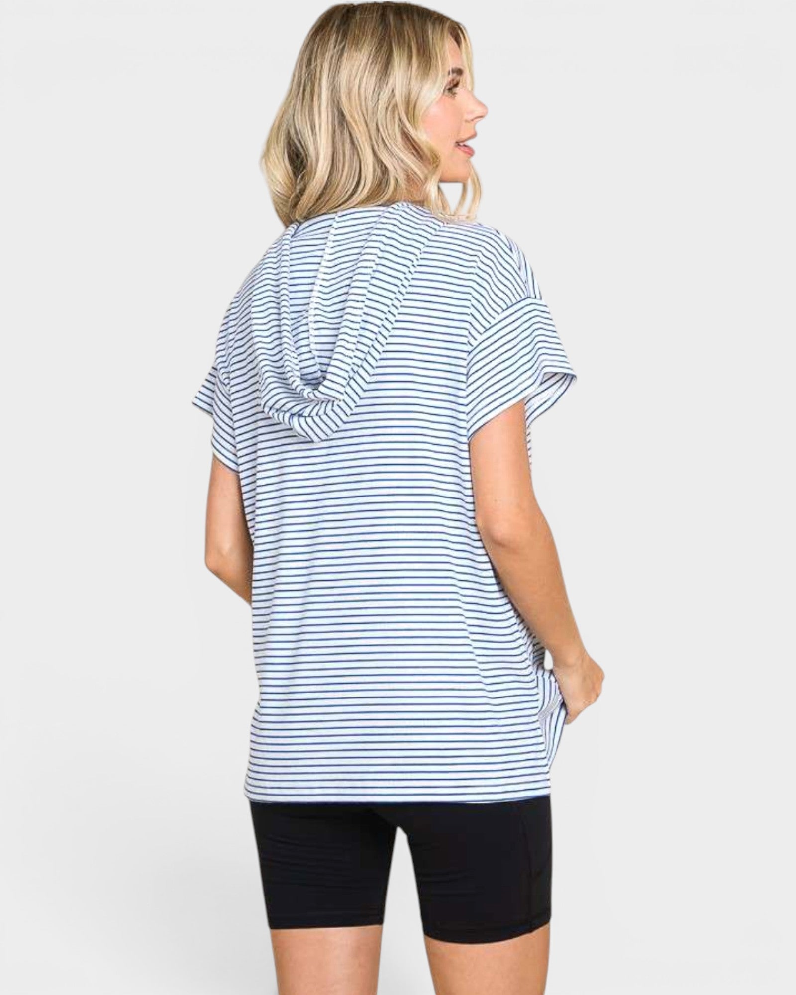 A woman shown from the back wearing a loose short-sleeve top with thin blue and white horizontal stripes, paired with black bike shorts, against a light gray studio background.