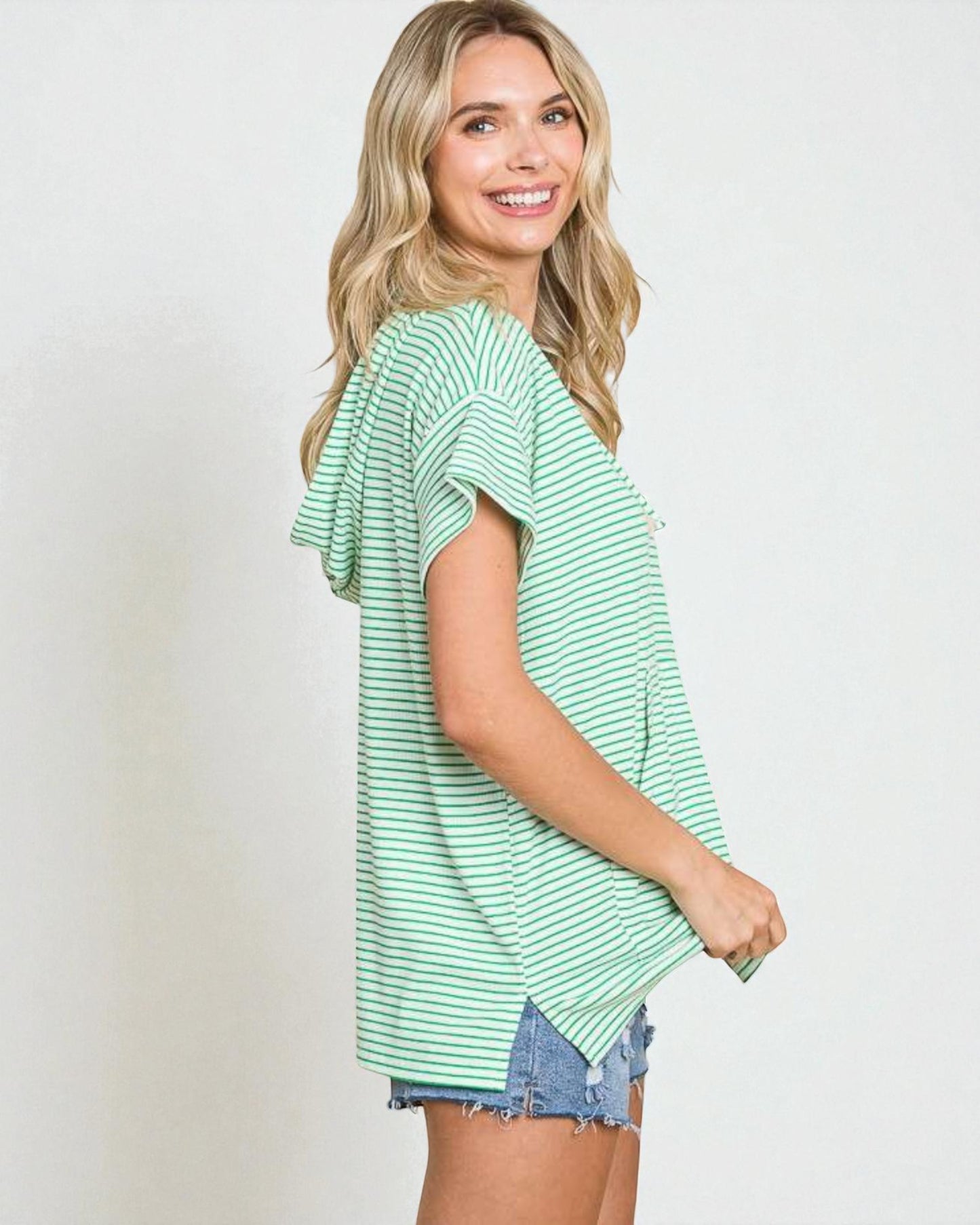 Woman wearing a green and white striped shirt with denim shorts on a plain background