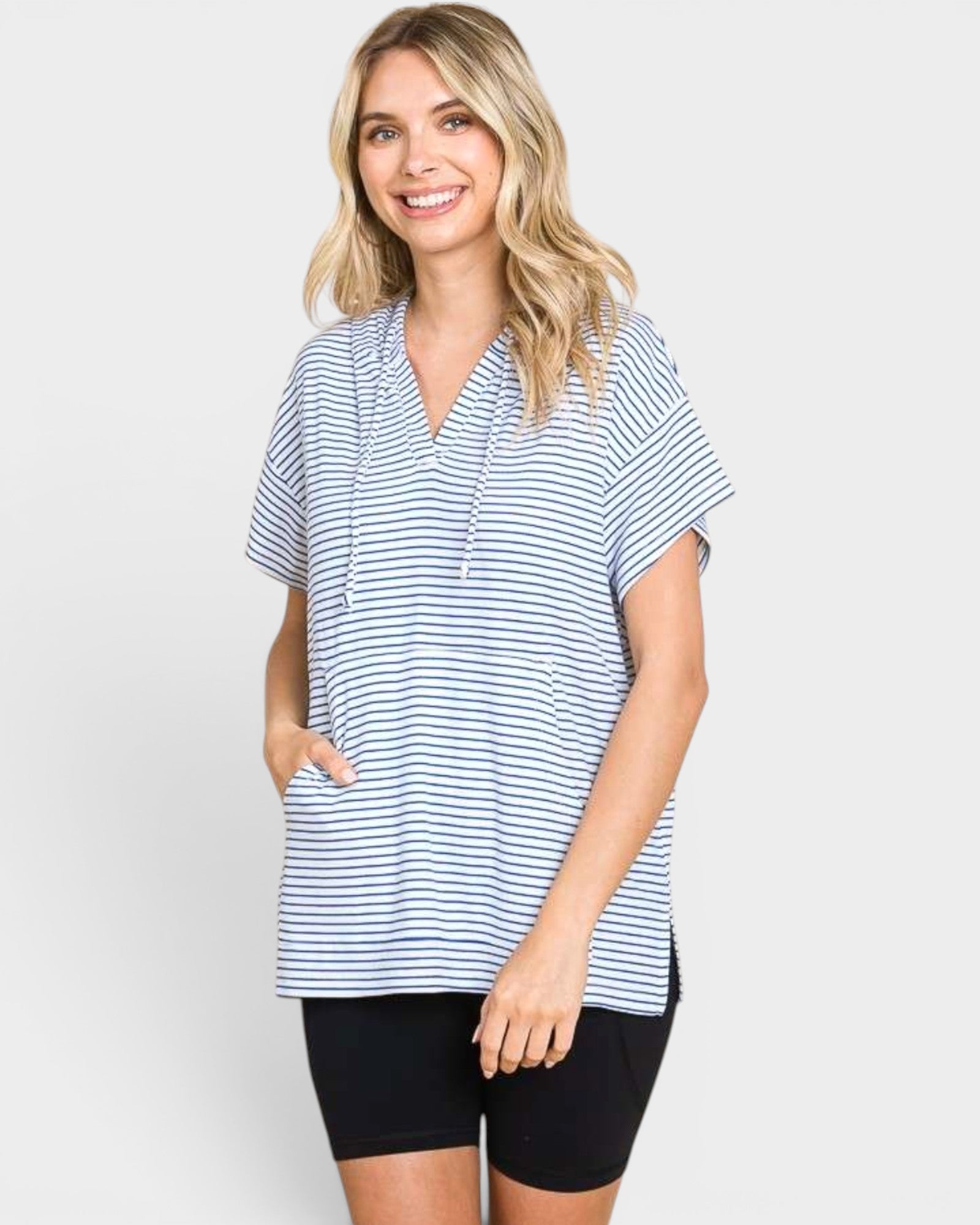 A woman modeling a short-sleeve, v-neck striped top with black bike shorts against a light gray studio background.