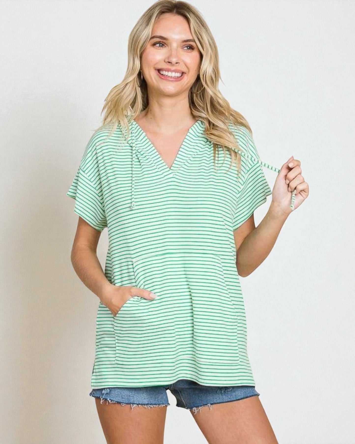 Woman wearing a green striped shirt and denim shorts on a plain background