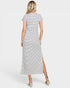 A woman shown from the back wearing a short-sleeve, midi-length dress with thin horizontal black and white stripes and a side slit, paired with beige wedge sandals, against a light gray studio background.