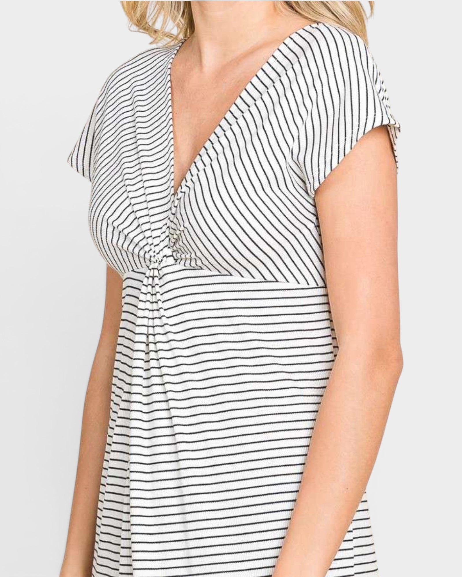 A close-up of a woman wearing a white short-sleeve dress with thin black vertical stripes, featuring a V-neckline and a gathered waist detail.