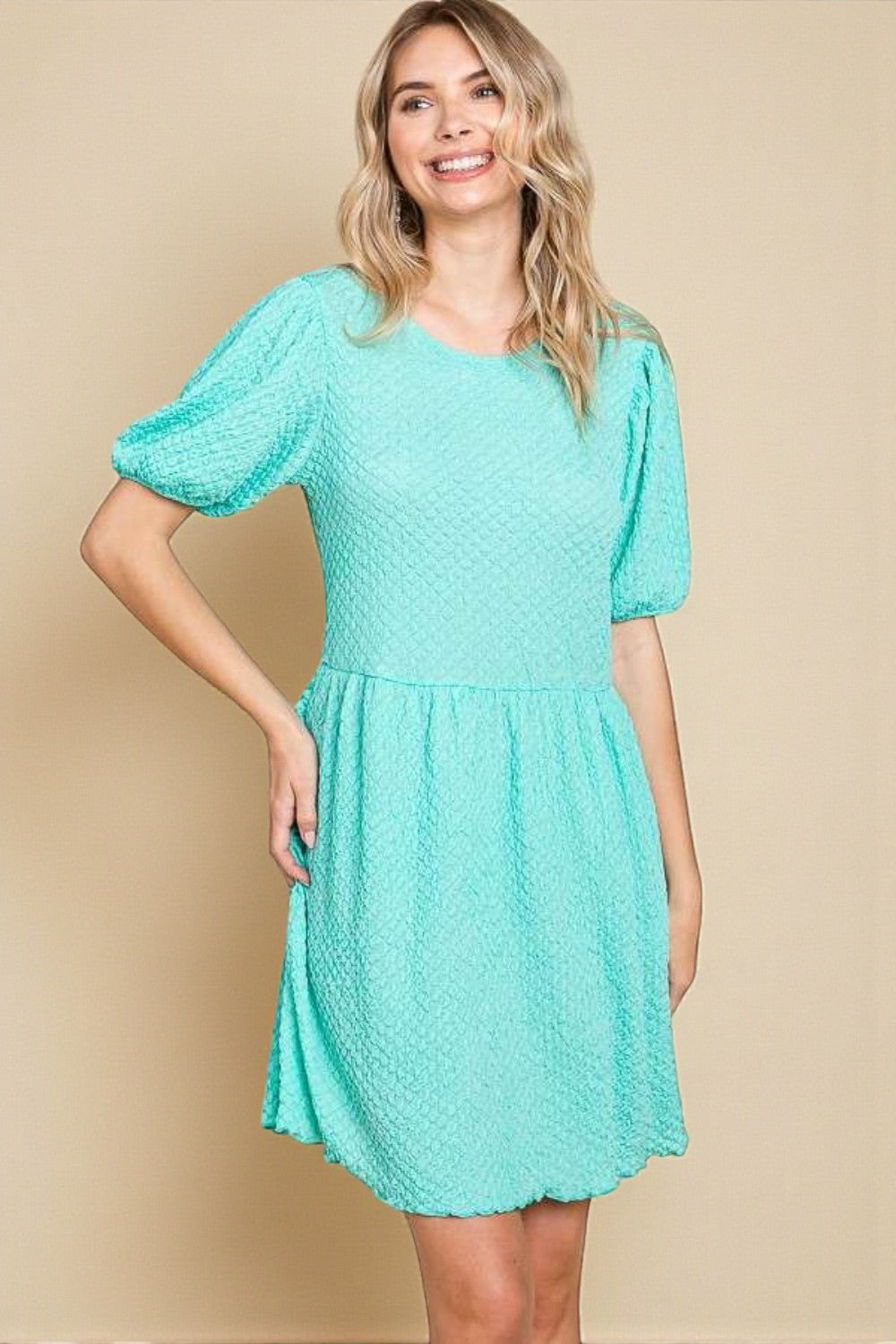 Woman wearing a teal dress against a beige background