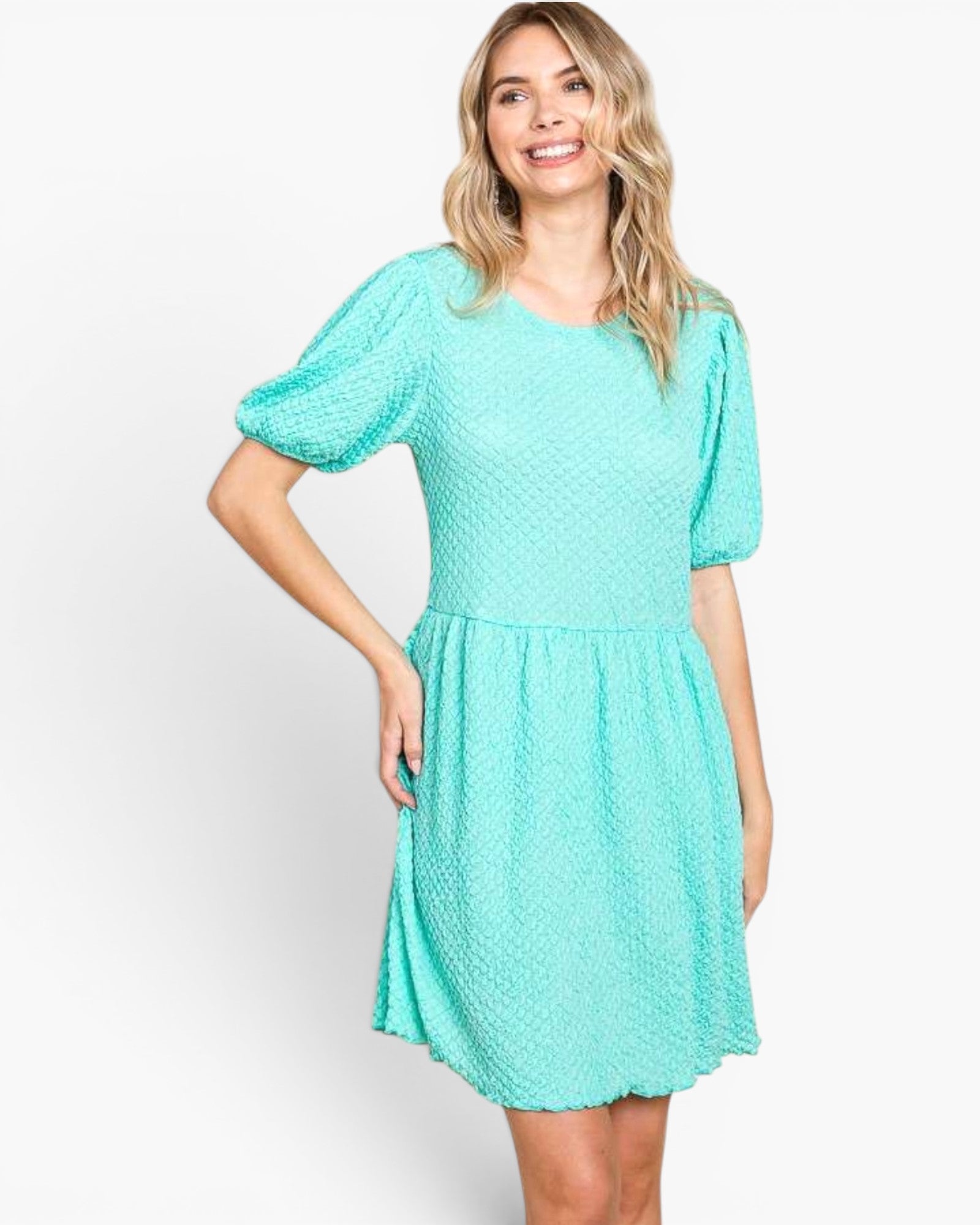 A woman modeling a short-sleeve, knee-length dress in a bright mint green or aqua color with a textured, dotted fabric pattern. The dress features a round neckline, puffed short sleeves, and a gathered skirt, shown against a plain light gray studio background.