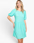 A woman modeling a short-sleeve, knee-length dress in a bright mint green or aqua color with a textured, dotted fabric pattern. The dress features a round neckline, puffed short sleeves, and a gathered skirt, shown against a plain light gray studio background.
