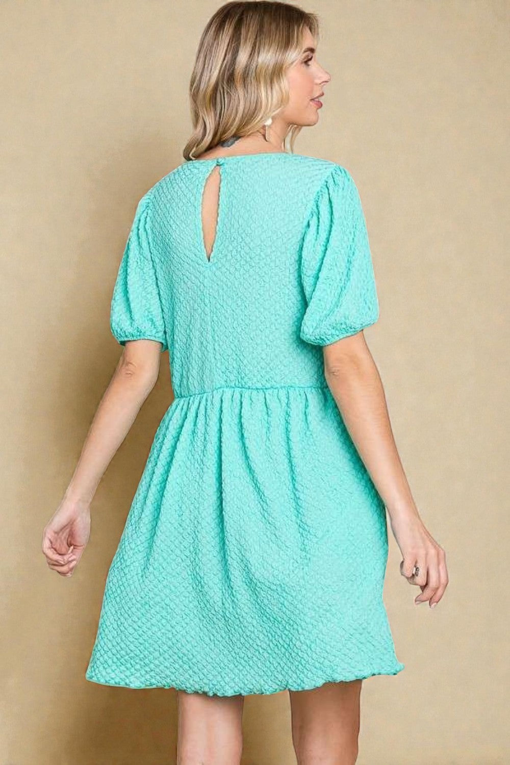 Woman wearing a teal dress against a beige background