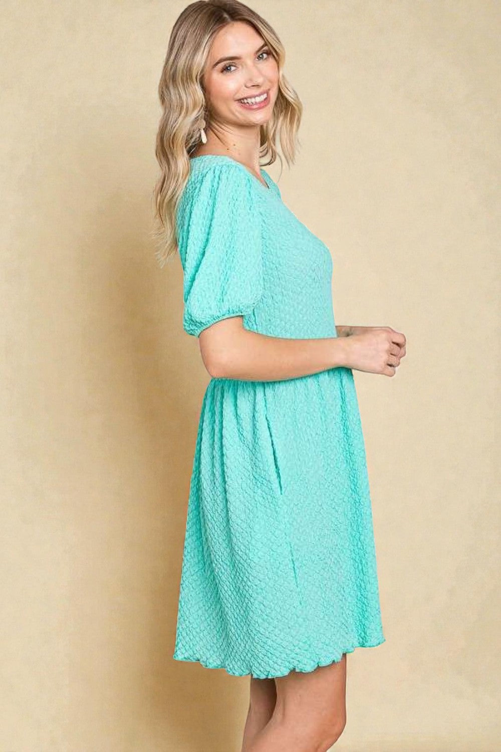 Woman wearing a teal dress against a beige background