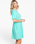 A woman modeling a short-sleeve, knee-length dress in a bright mint green or aqua color with a textured, dotted fabric pattern, set against a plain white studio background.