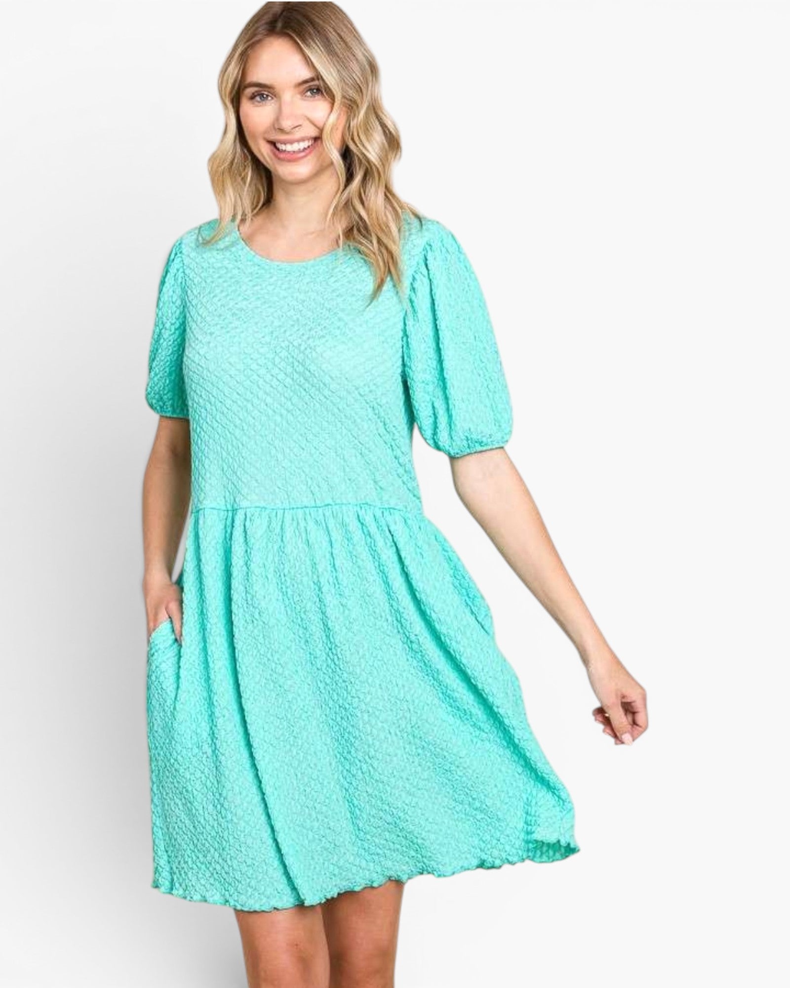 A woman wearing a short-sleeve, knee-length aqua green textured dress with puff sleeves and side pockets, photographed against a plain light gray studio background.