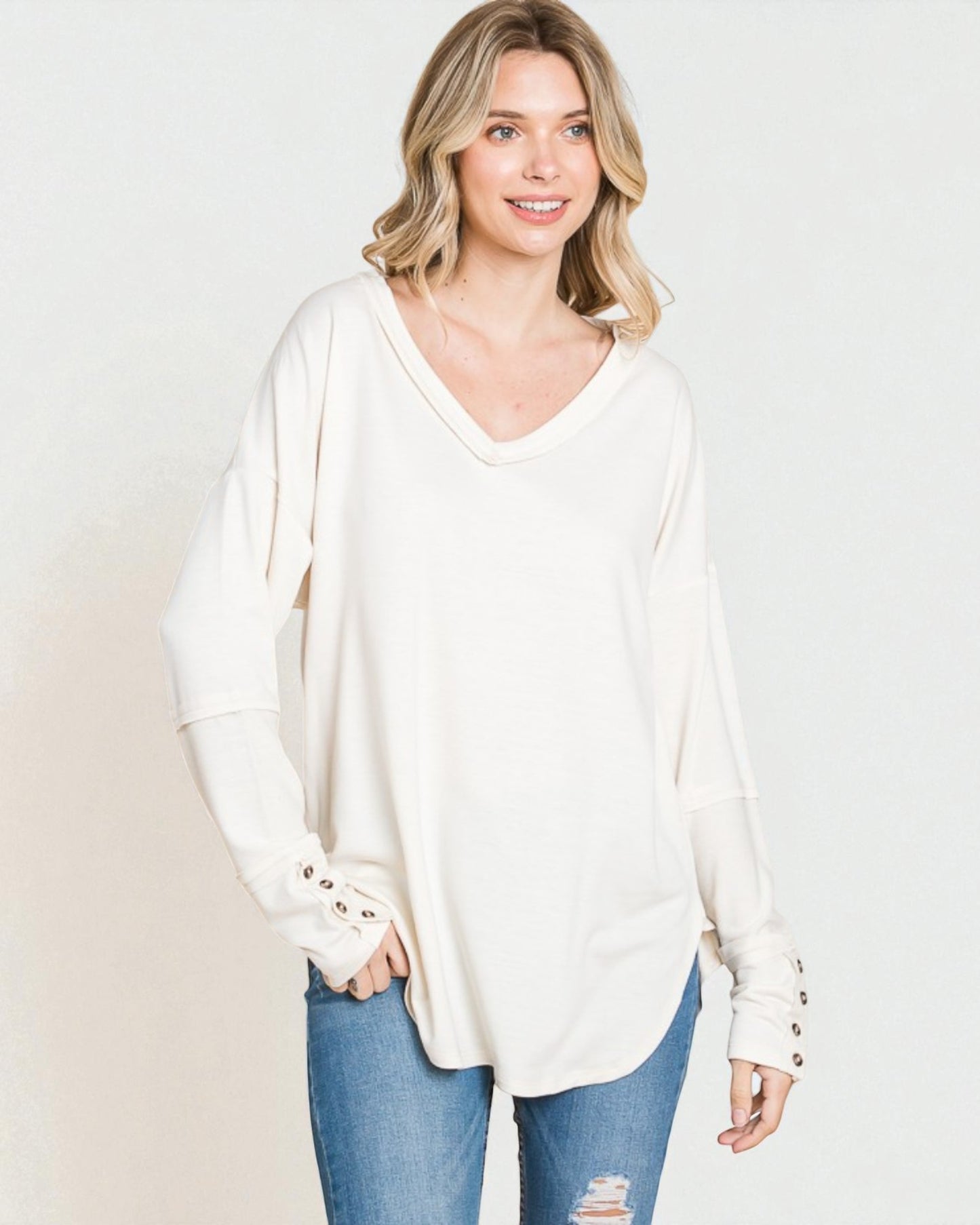 Woman wearing a white long-sleeve top with button details on a plain background