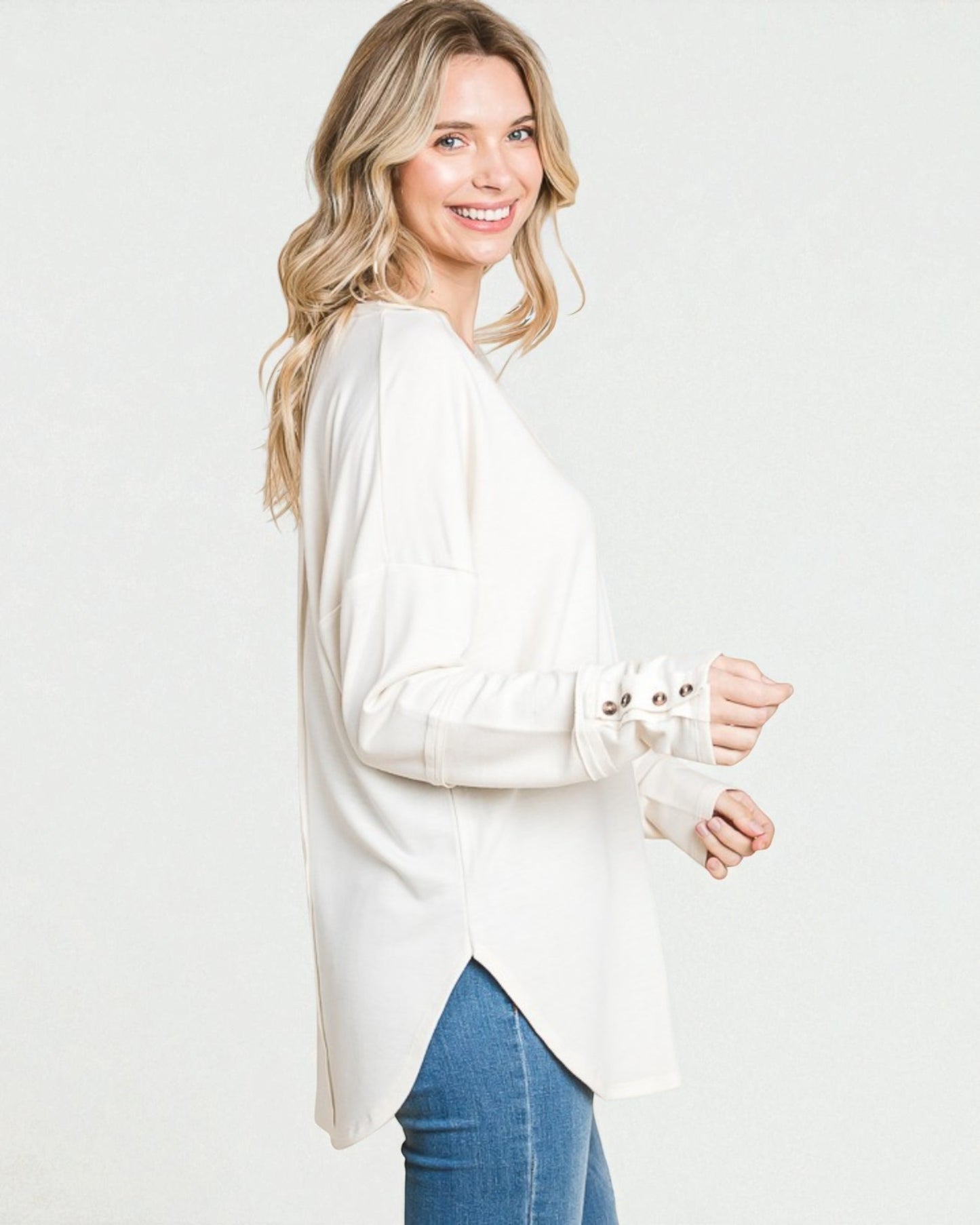 Woman wearing a white long-sleeve top and blue jeans on a plain background