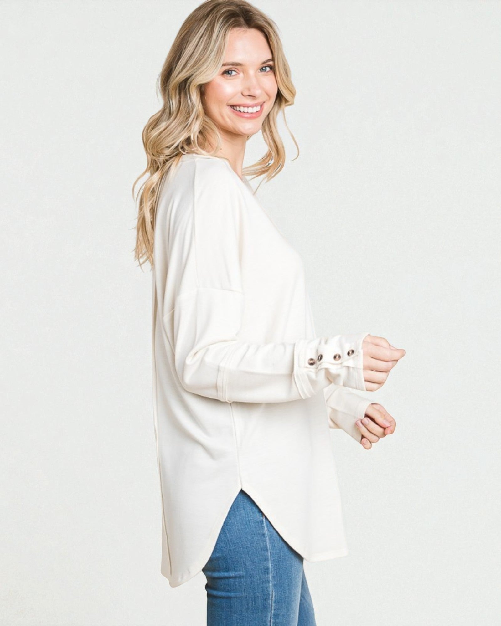 Woman wearing a white long-sleeve top and blue jeans on a plain background