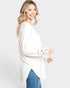 Woman wearing a white sweater and blue jeans on a plain background
