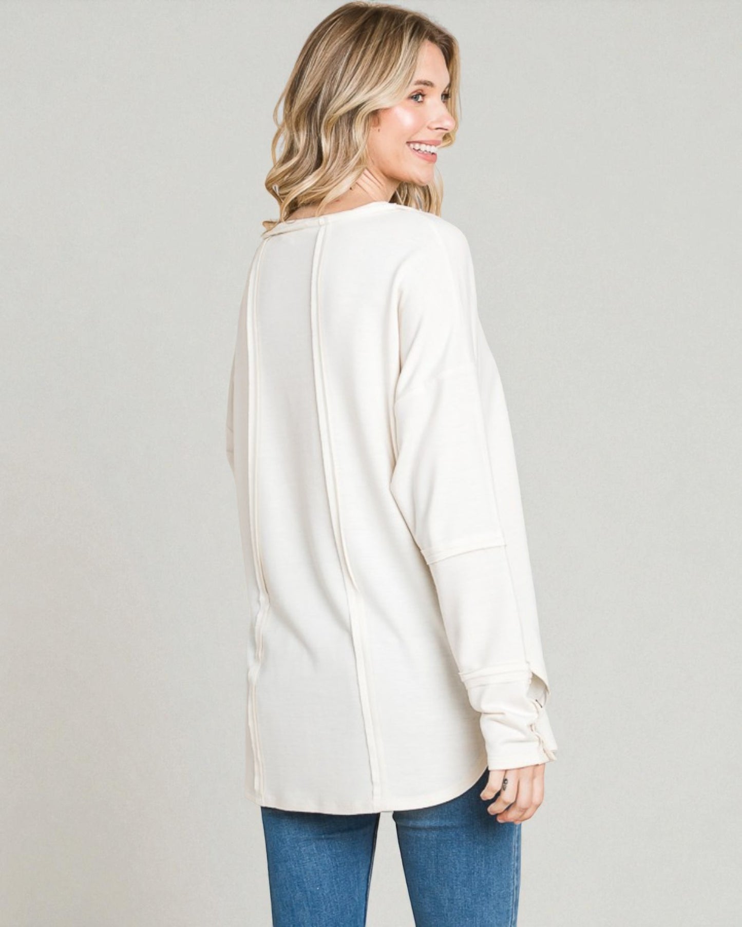 Woman wearing a white cardigan and blue jeans on a plain background