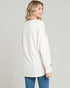 Woman wearing a white cardigan and blue jeans on a plain background