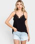Woman wearing a black lace-trimmed camisole and denim shorts on a plain background