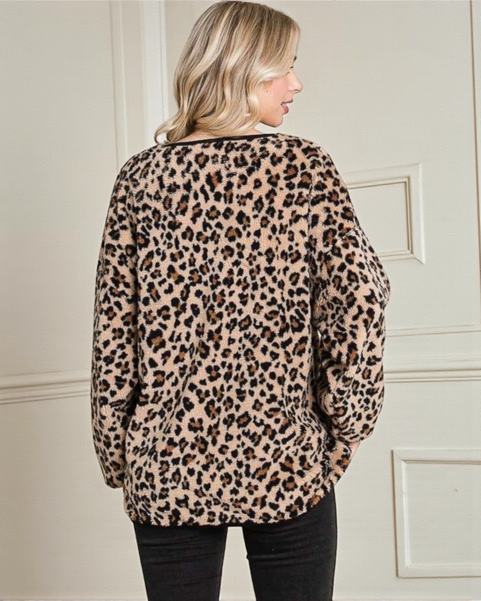 Person wearing a leopard print sweater against a neutral wall.