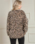 Person wearing a leopard print sweater against a neutral wall.