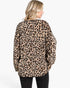 A woman shown from the back wearing a beige leopard-print fleece sweater with black pants, photographed against a plain white studio background.