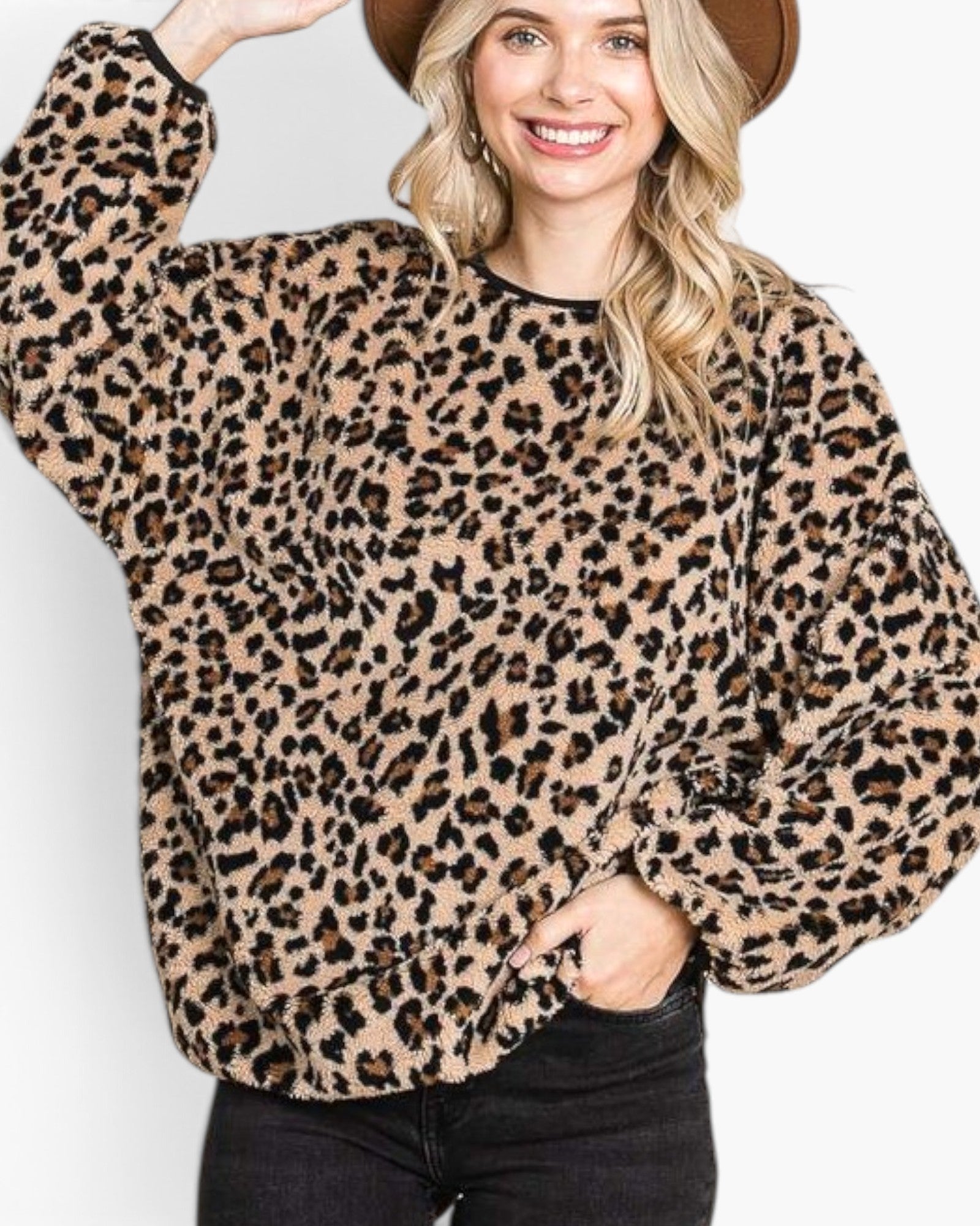 A woman wearing a fuzzy leopard-print long-sleeve top with black trim, paired with black jeans and a brown hat, against a plain white background.